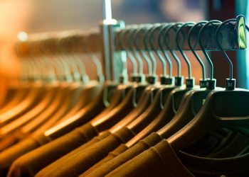 A row of neatly arranged clothes hanging on a rack with wooden hangers.