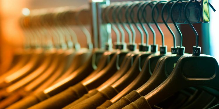 A row of neatly arranged clothes hanging on a rack with wooden hangers.