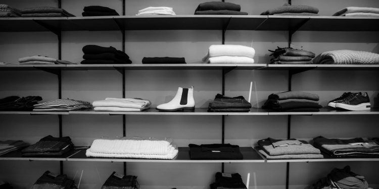 Neatly folded clothing and shoes displayed on shelves in a boutique setting.