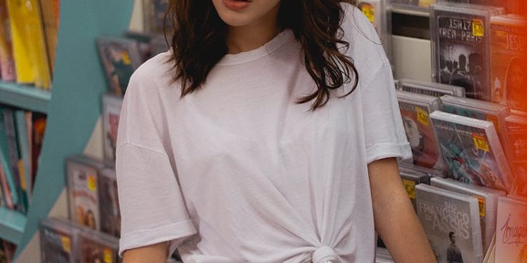 Fashionable woman posing in a music store wearing a white t-shirt and jeans.