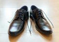 A pair of shiny, elegant black leather dress shoes with laces on a wooden floor.