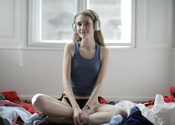 Young woman enjoying music on headphones in a light-filled, messy room.