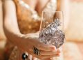 A woman in a gold dress holds a wine glass filled with crystals, exuding luxury and sophistication.