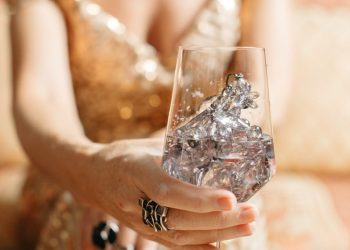 A woman in a gold dress holds a wine glass filled with crystals, exuding luxury and sophistication.