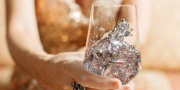 A woman in a gold dress holds a wine glass filled with crystals, exuding luxury and sophistication.