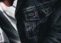 A textured close-up of a denim jacket featuring buttons and label details on a casual outfit.
