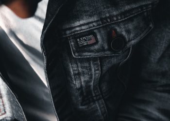 A textured close-up of a denim jacket featuring buttons and label details on a casual outfit.