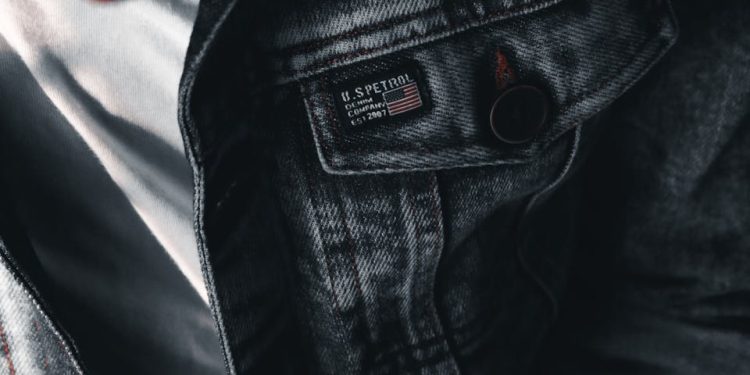 A textured close-up of a denim jacket featuring buttons and label details on a casual outfit.