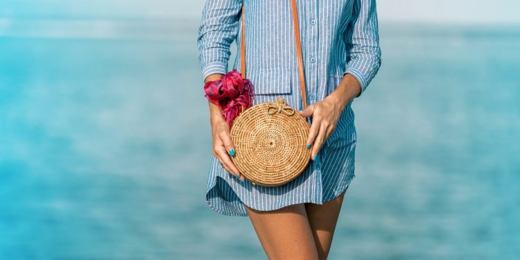 woman wearing blue and white striped dress shirt dress with brown wicker crossbody bag near sea at daytime